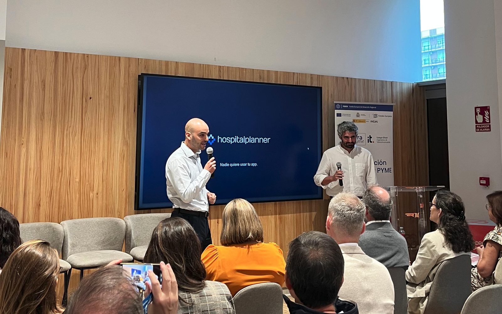 Sergio Robles y Miguel Ocaña, cofundadores de HospitalPlanner, ante el público del Startup Showcase de HealthTech Innovation, en el Madrid Health Hub, con la diapositiva de portada Nadie quiere usar tu app